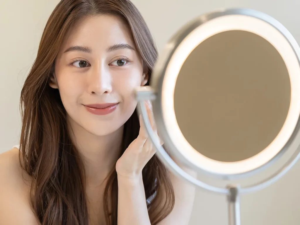 Młoda Koreanka przyglądająca się skórze twarzy w lustrze