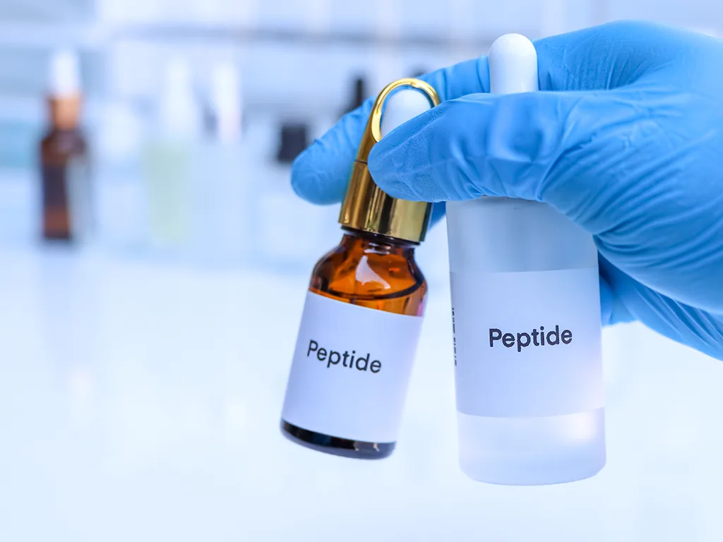 Kobieca dłoń trzyma dwie fiolki serum z peptydami