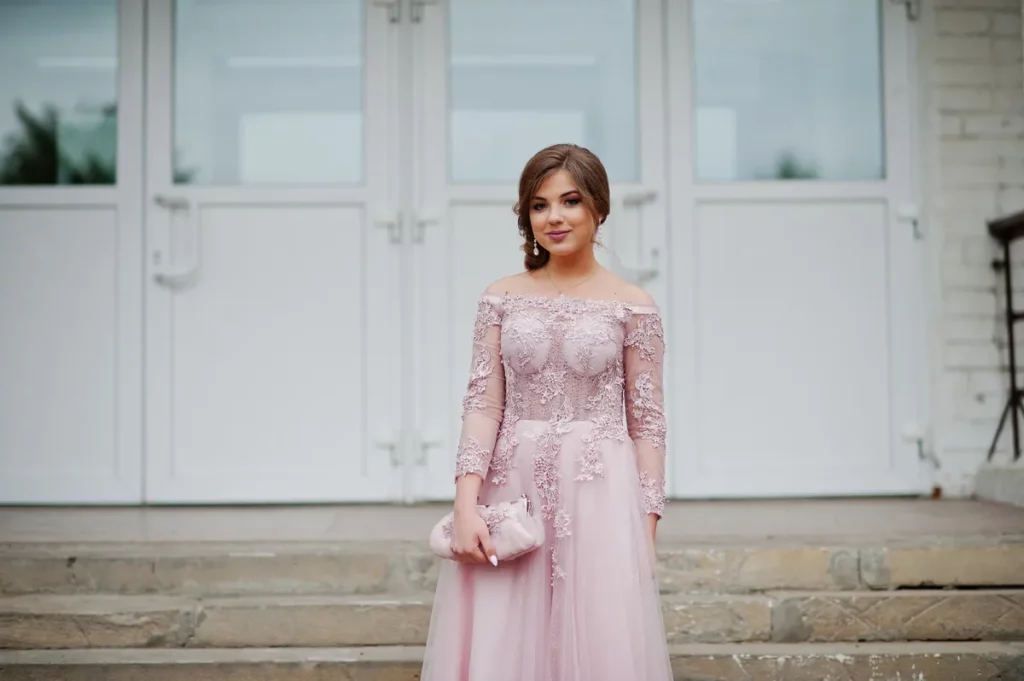 Młoda dziewczyna stoi przed wejściem do szkoły w różowej sukience i w subtelnym makijażu Źródło: Adobe Stock